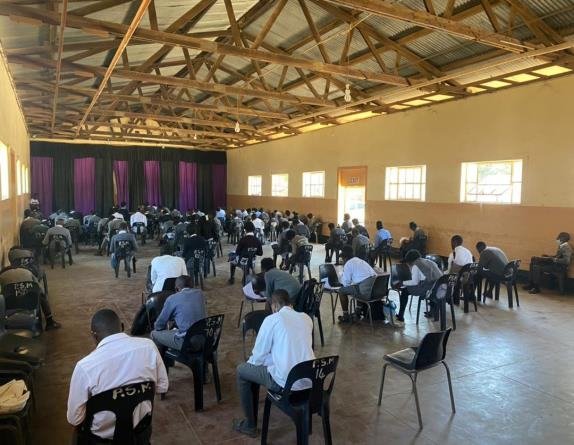 Secondary school pupils sitting spaced apart at desks in a large school hall during an examination